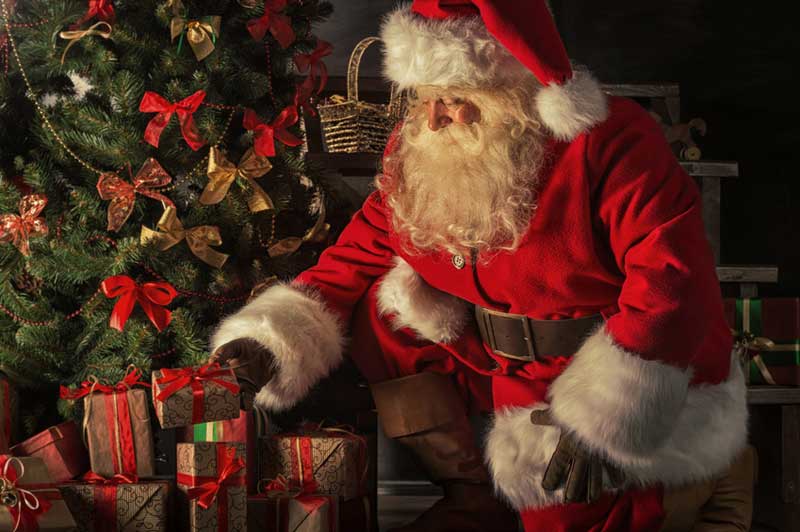 Santa kneeling and placing a gift under a tree